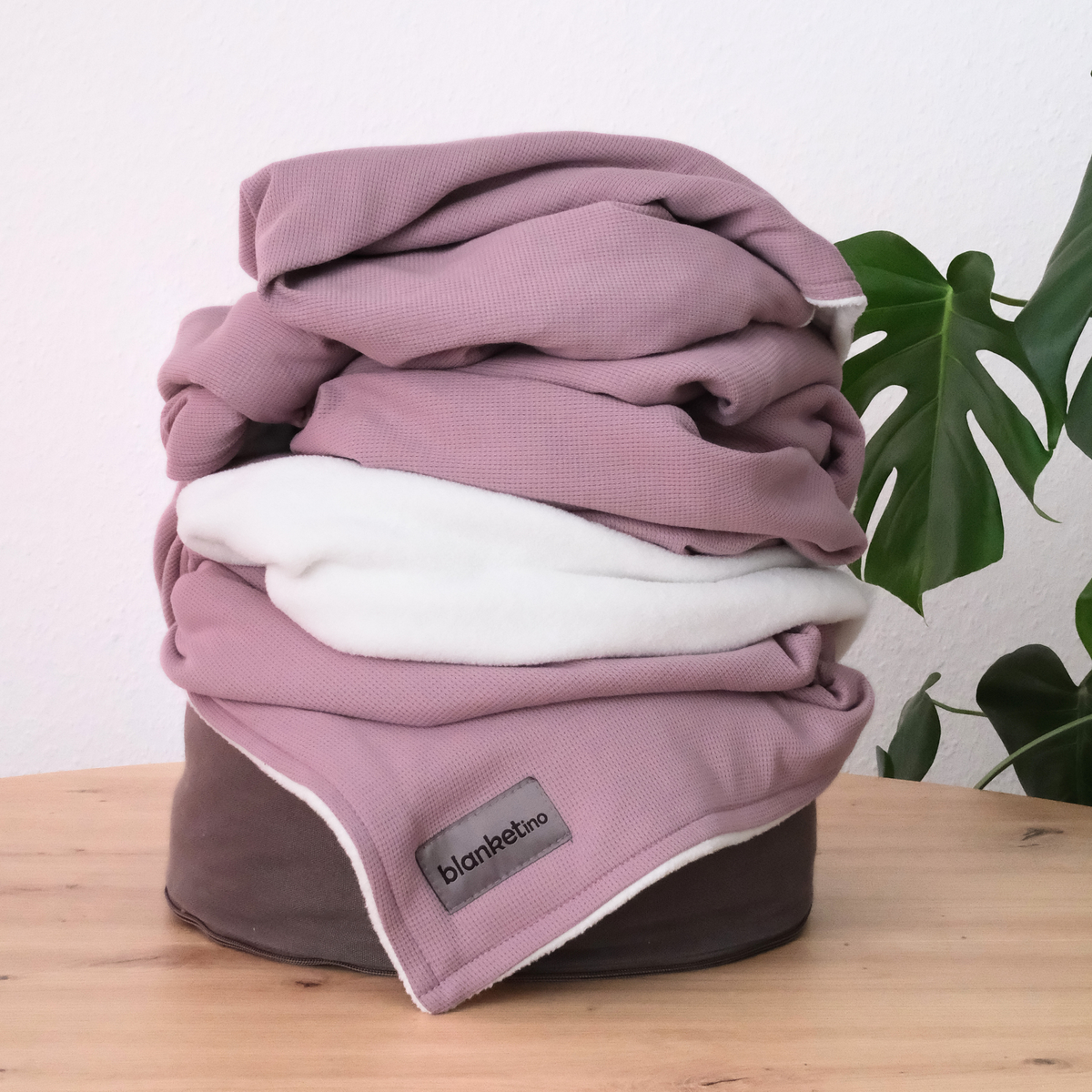 Sommerdecke aus 100% Baumwolle von blanketino.de, beerefarbene Decke gefaltet auf einem Pouf, ideal für warme Tage.