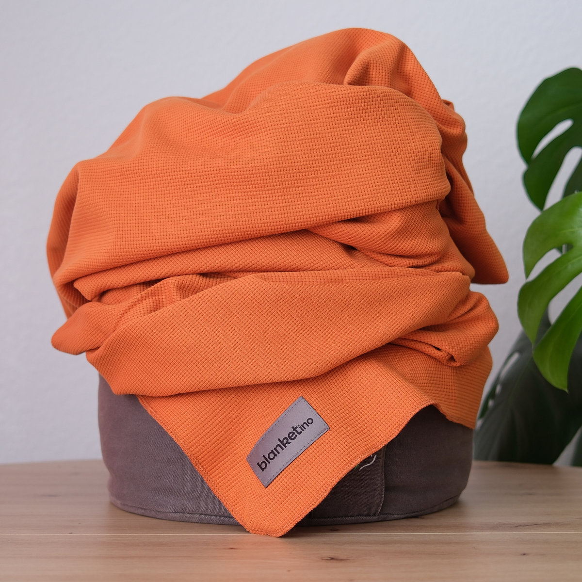 Leichte Baumwoll-Sommerdecke in Orange, 150 x 210 cm, aus 100% Baumwolle von blanketino.de auf einem Pouf.