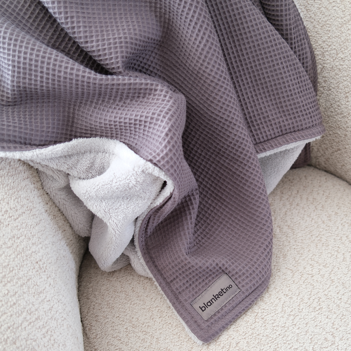 Weiche Kuscheldecke "Vollkommen" in Gletschergrau von blanketino.de, flauschige Fleece-Rückseite auf einem Sessel.