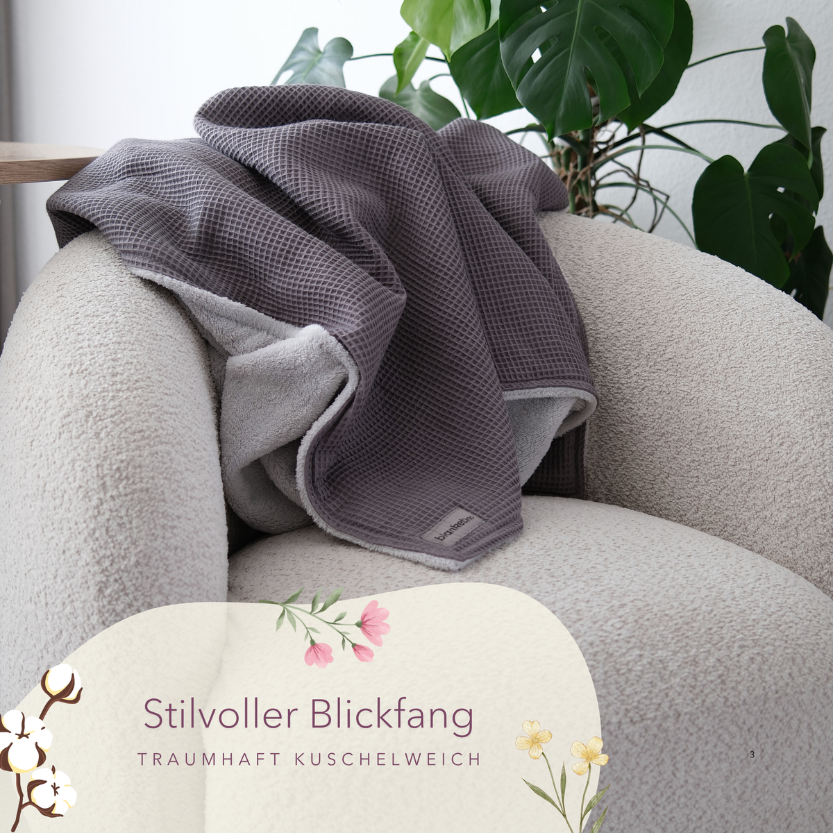 Weiche Kuscheldecke "Vollkommen" in Gletschergrau von blanketino.de auf einem beigen Sessel drapiert.