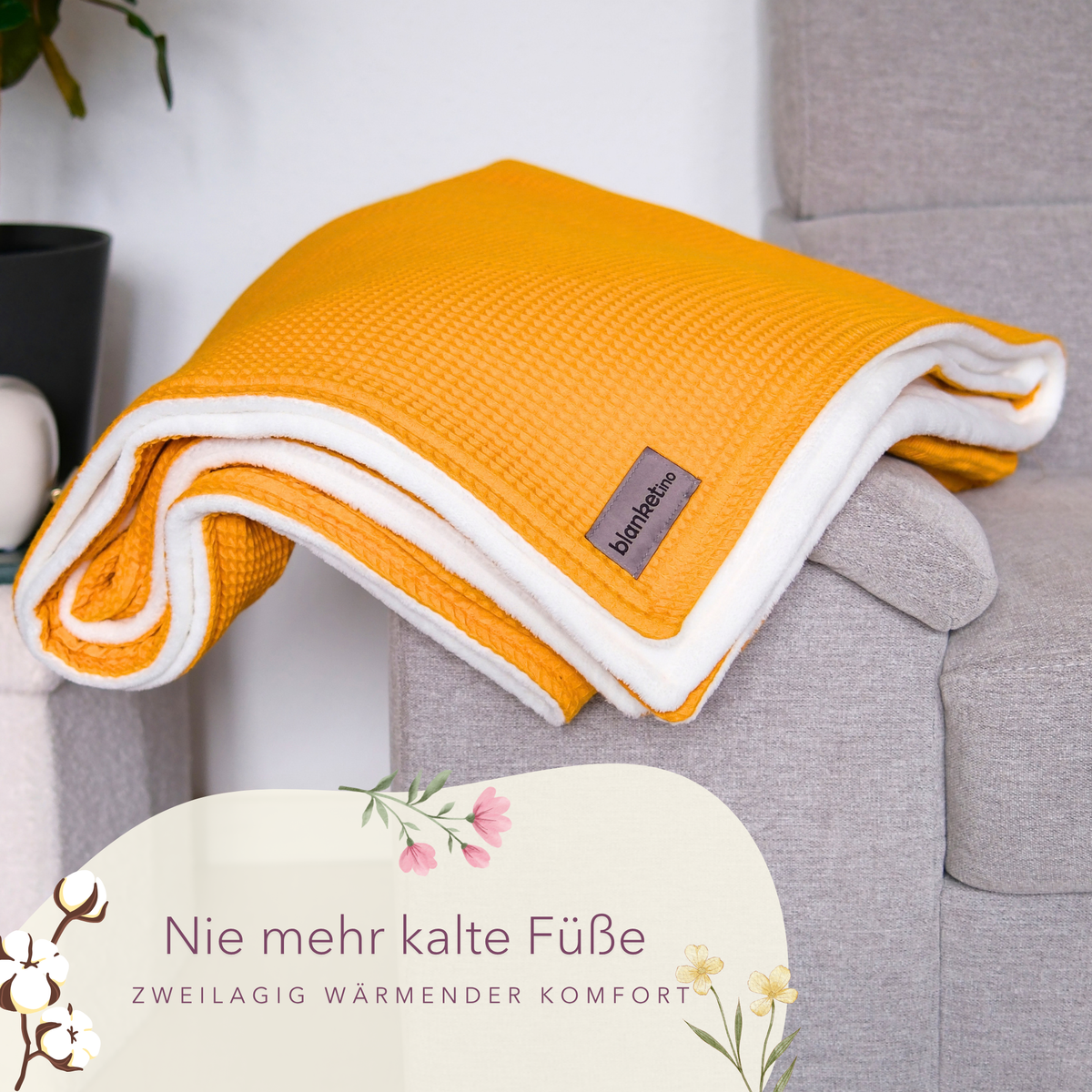 Weiche Kuscheldecke "Vollkommen" in Ocker Gelb und Sandweiß, gefaltet auf einem Sofa, aus Waffelpique von blanketino.de