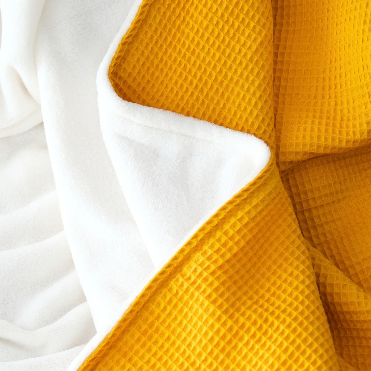 Weiche Kuscheldecke "Vollkommen" in Ocker Gelb mit Waffelpique-Design und weißer Rückseite, perfekt für gemütliche Stunden.
