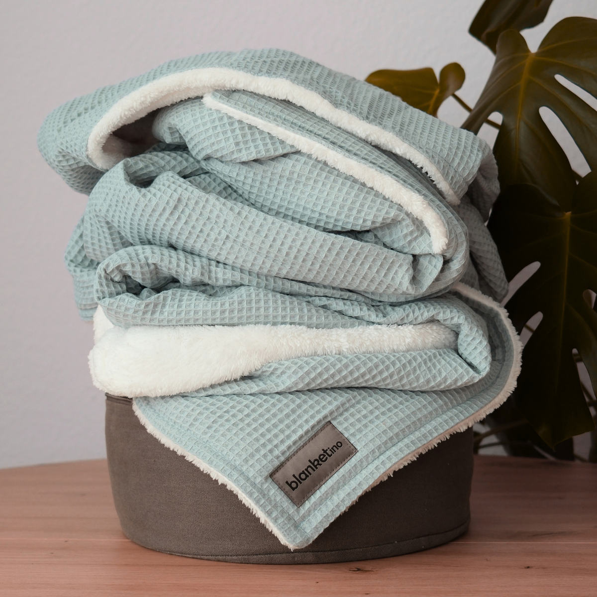 Weiche Kuscheldecke "Vollkommen" Mint von blanketino.de, gefaltet auf einem Pouf, mit Waffelpique-Struktur, ideal für gemütliche Stunden.