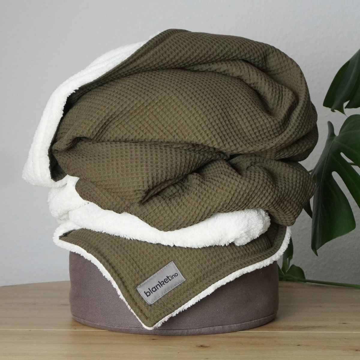 Weiche Kuscheldecke "Vollkommen" von blanketino.de, waffelpique in Waldgrün, gefaltet auf einem Pouf.