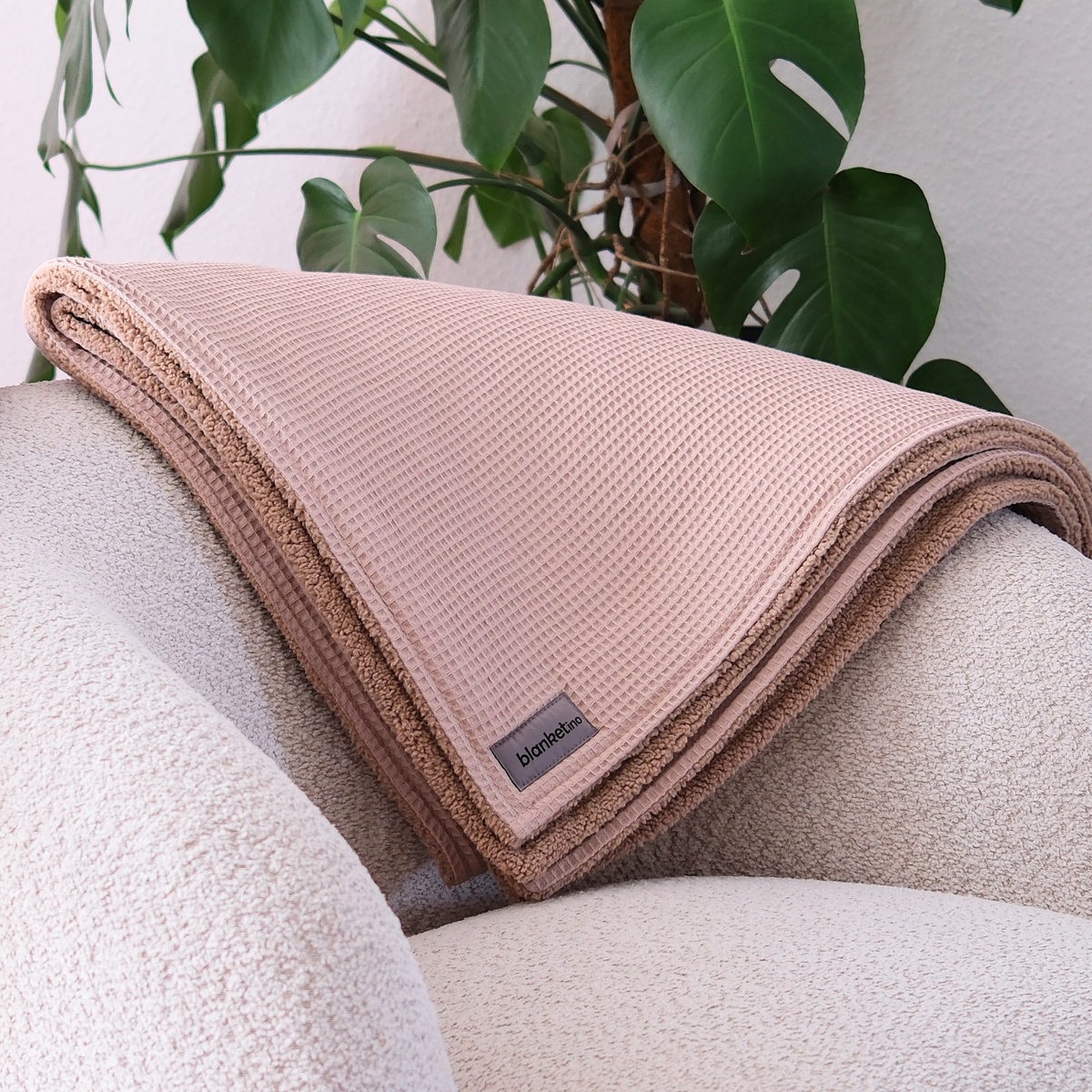 Weiche Kuscheldecke mit Teddy-Fleece in Beige, gefaltet auf einem Sessel, ideal zum gemütlichen Einkuscheln.